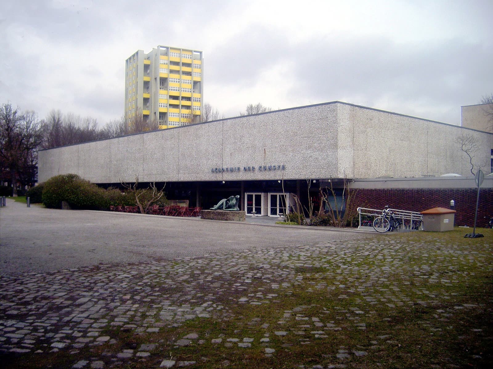 Low modernist concrete building of the Akademie der Künste on Hanseatenweg, with a cobbled forecourt and a tower block behind