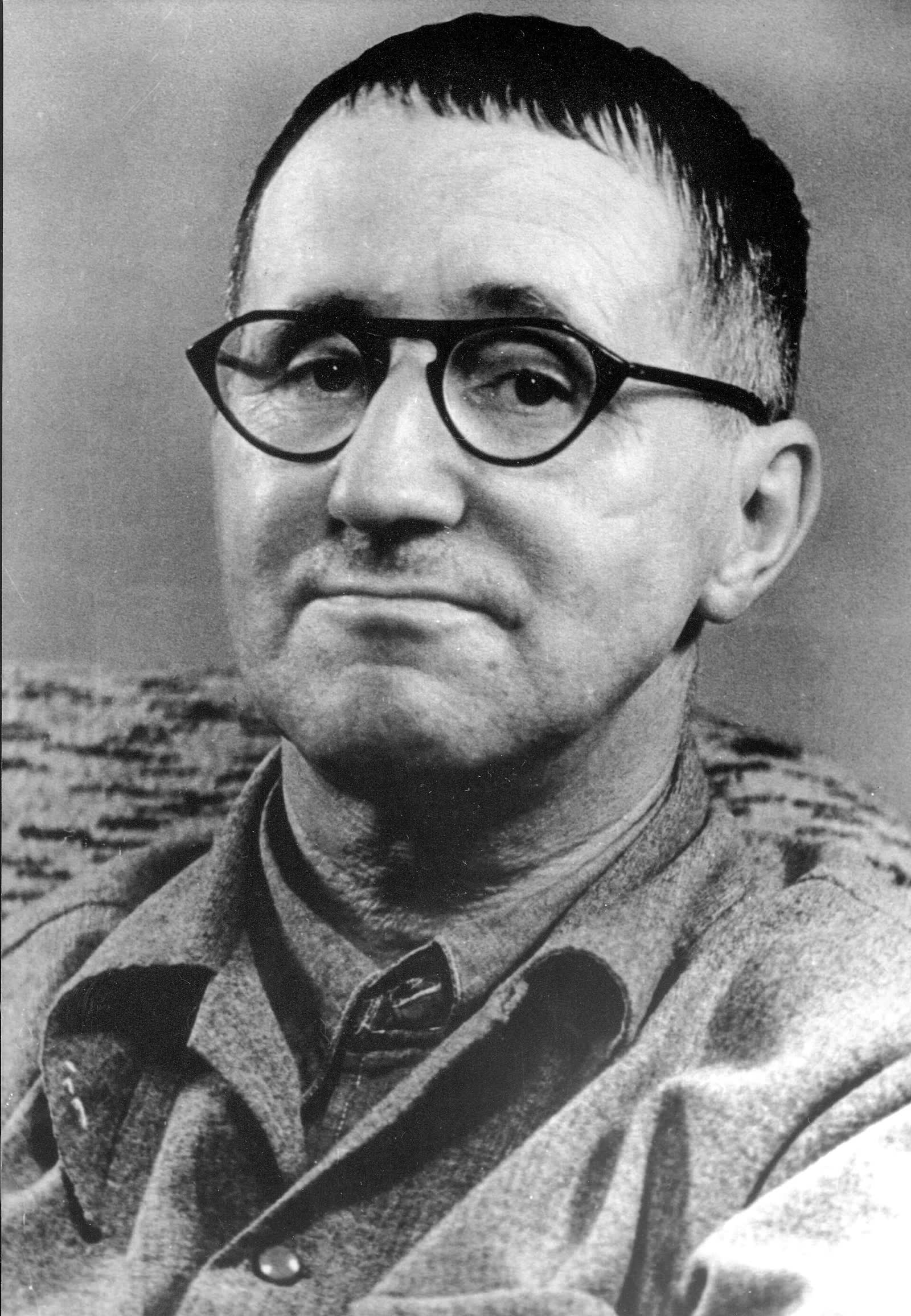 Black and white portrait of Bertolt Brecht with cropped hair and round glasses, in an open-necked shirt