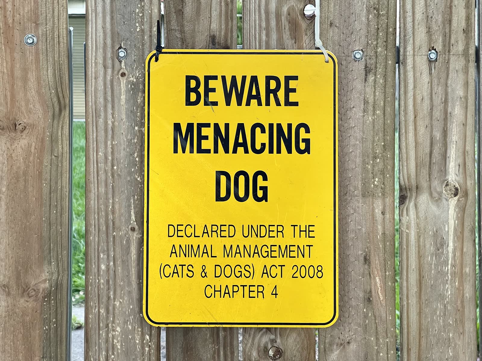 A Beware Menacing Dog warning sign on a property fence