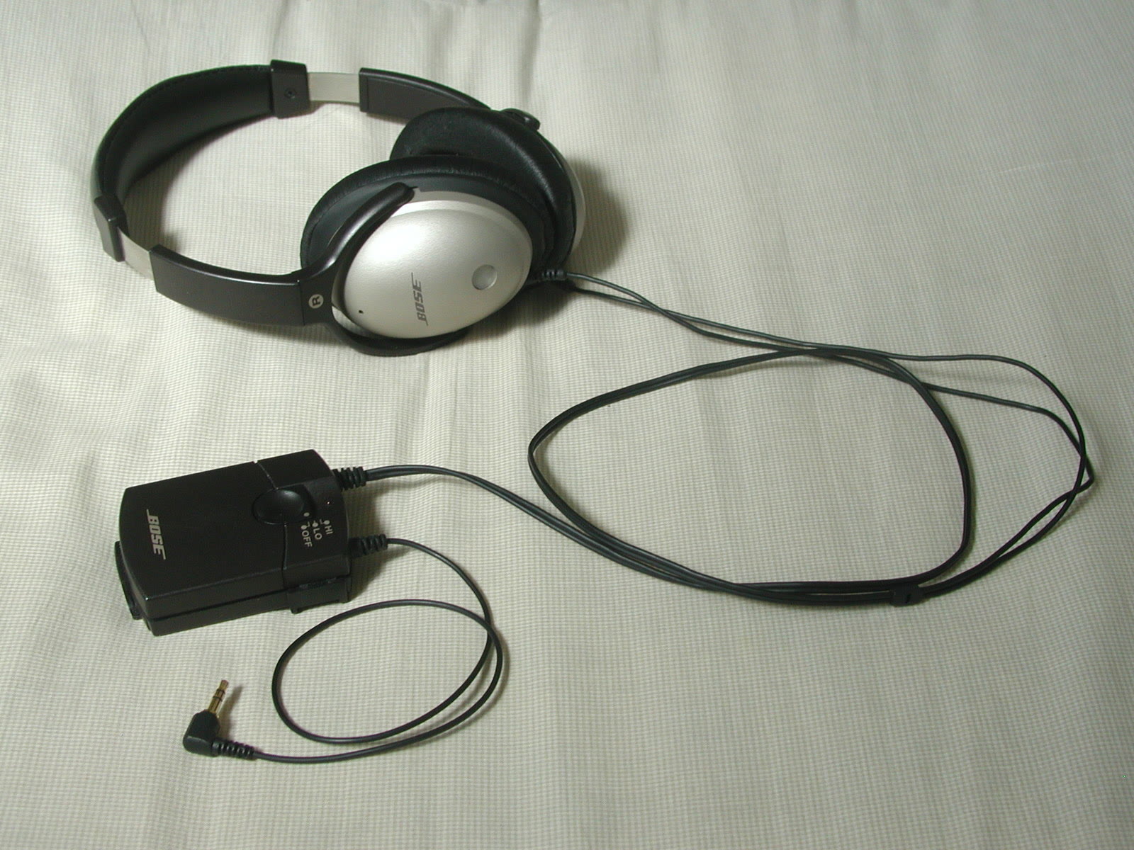 Silver and black Bose QuietComfort headphones with their cable and battery module on a white cloth