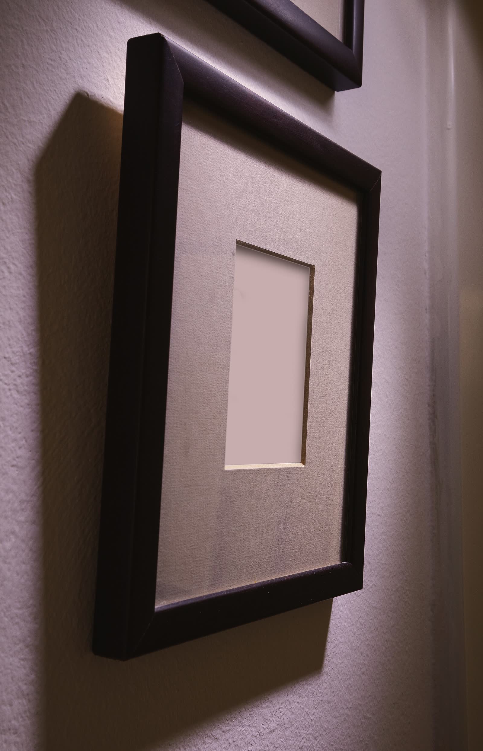 An empty wooden picture frame hanging on a wall, seen from the side