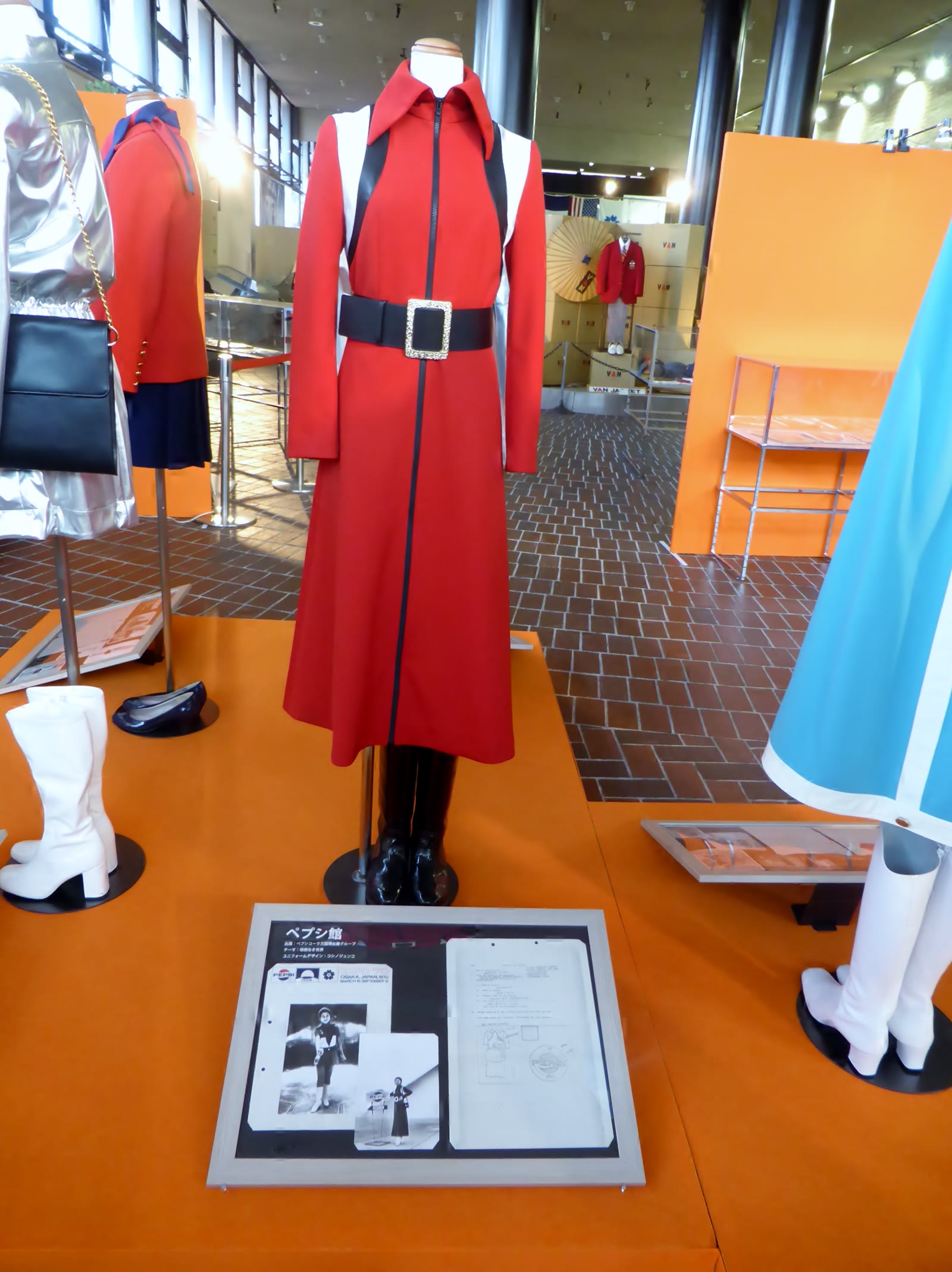 Red belted dress costume on a mannequin in a museum display with an orange floor