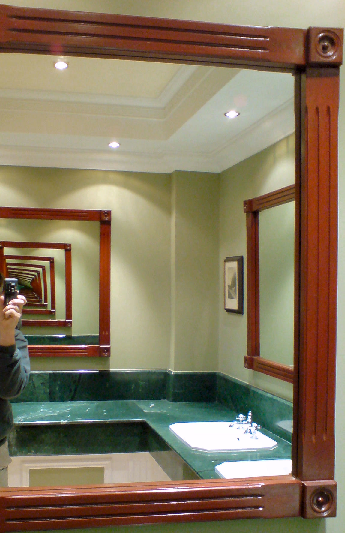 Two facing mirrors in a public washroom, producing a long corridor of repeated reflections