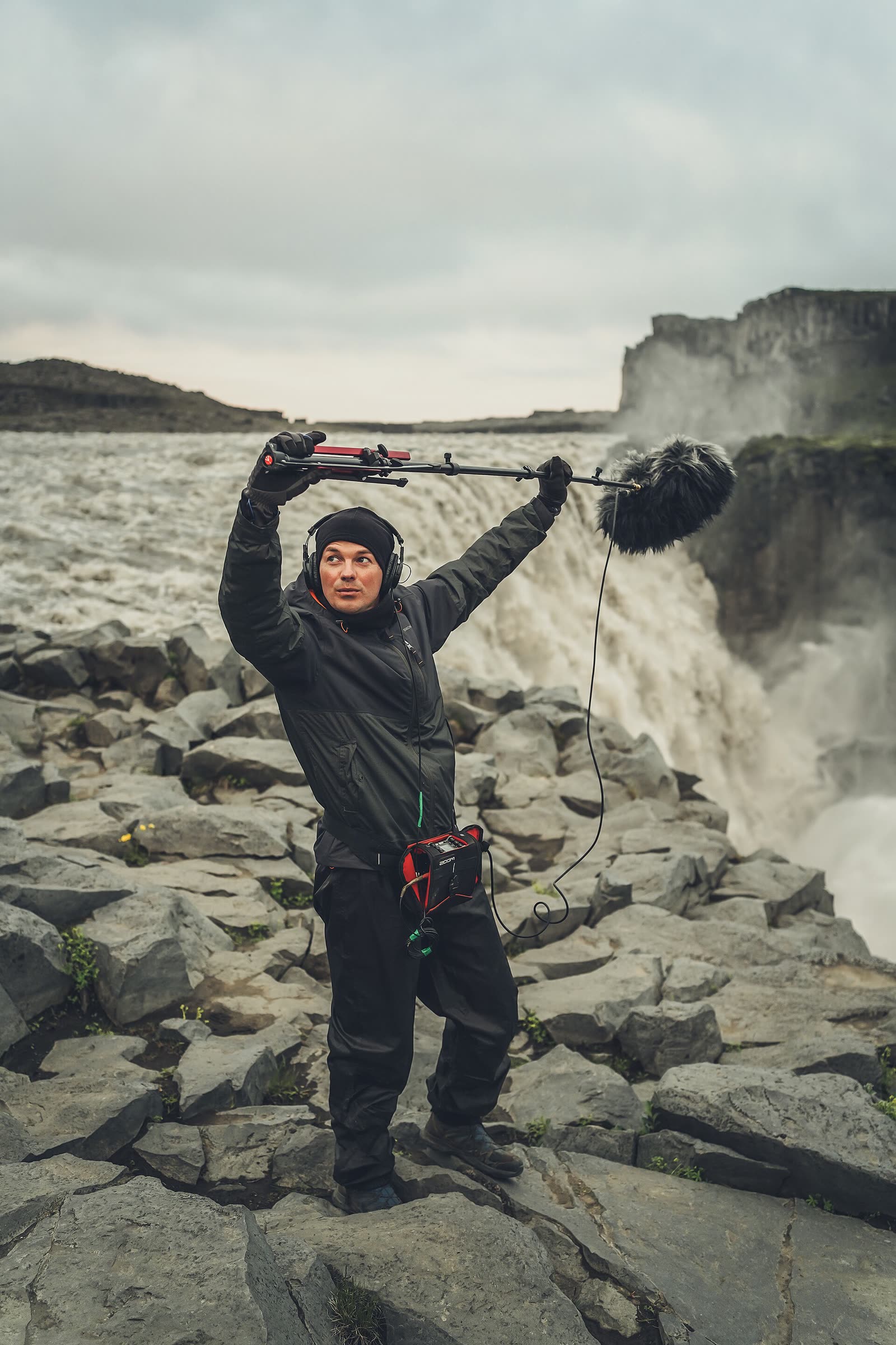 A field recordist with a microphone and recorder capturing sound beside Dettifoss waterfall in Iceland