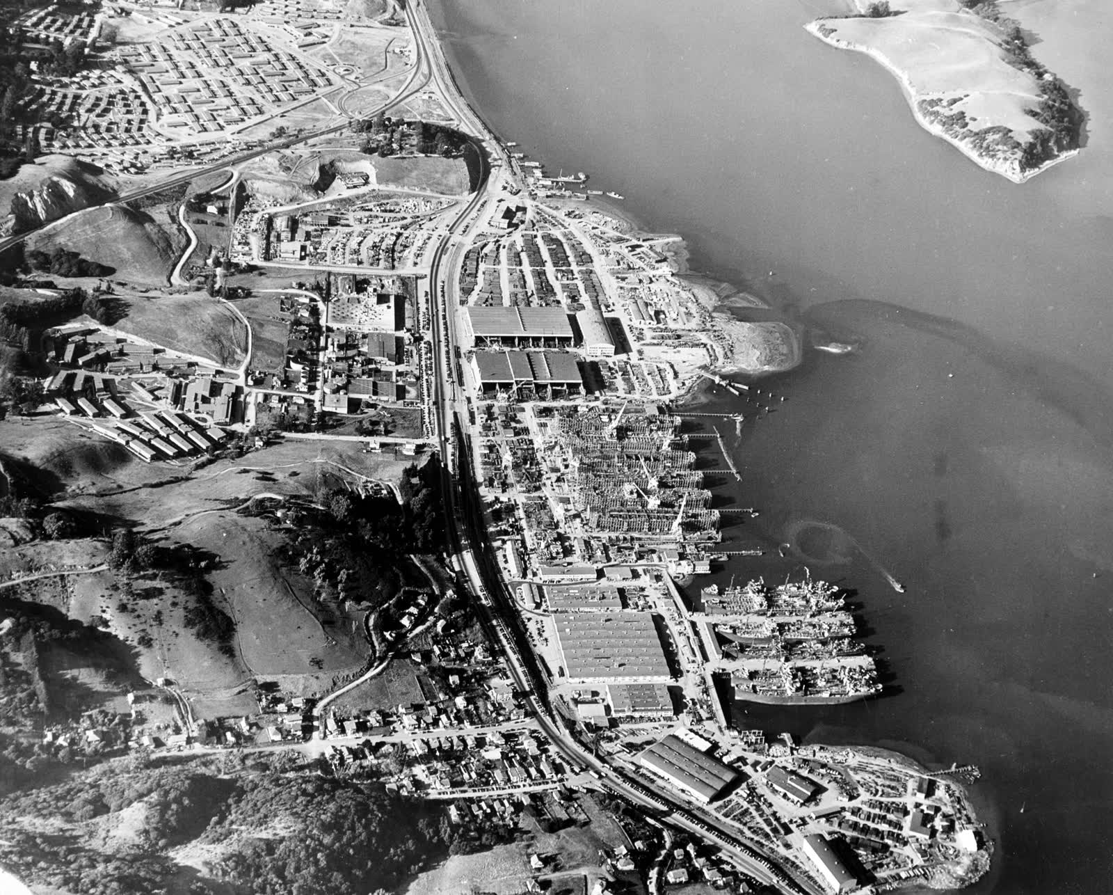 Aerial photograph of the Marinship shipyard in Sausalito with ships, slipways and shop buildings on the bay, 1944