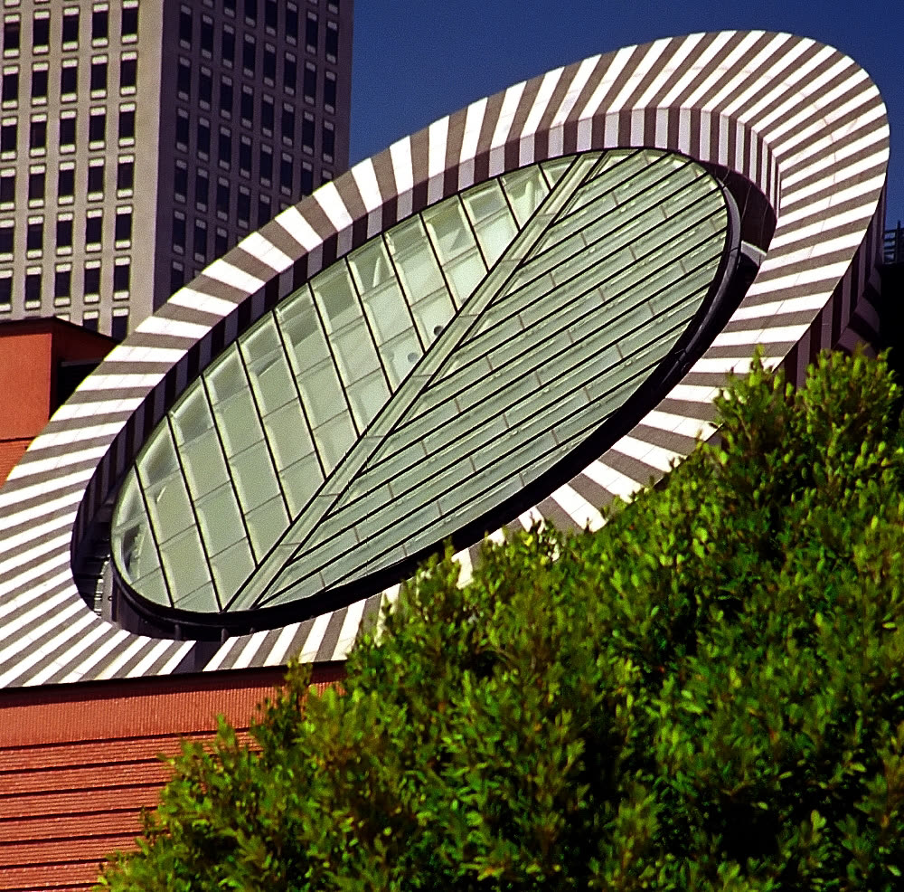The striped oval skylight tower of the San Francisco Museum of Modern Art against a blue sky, with trees in front