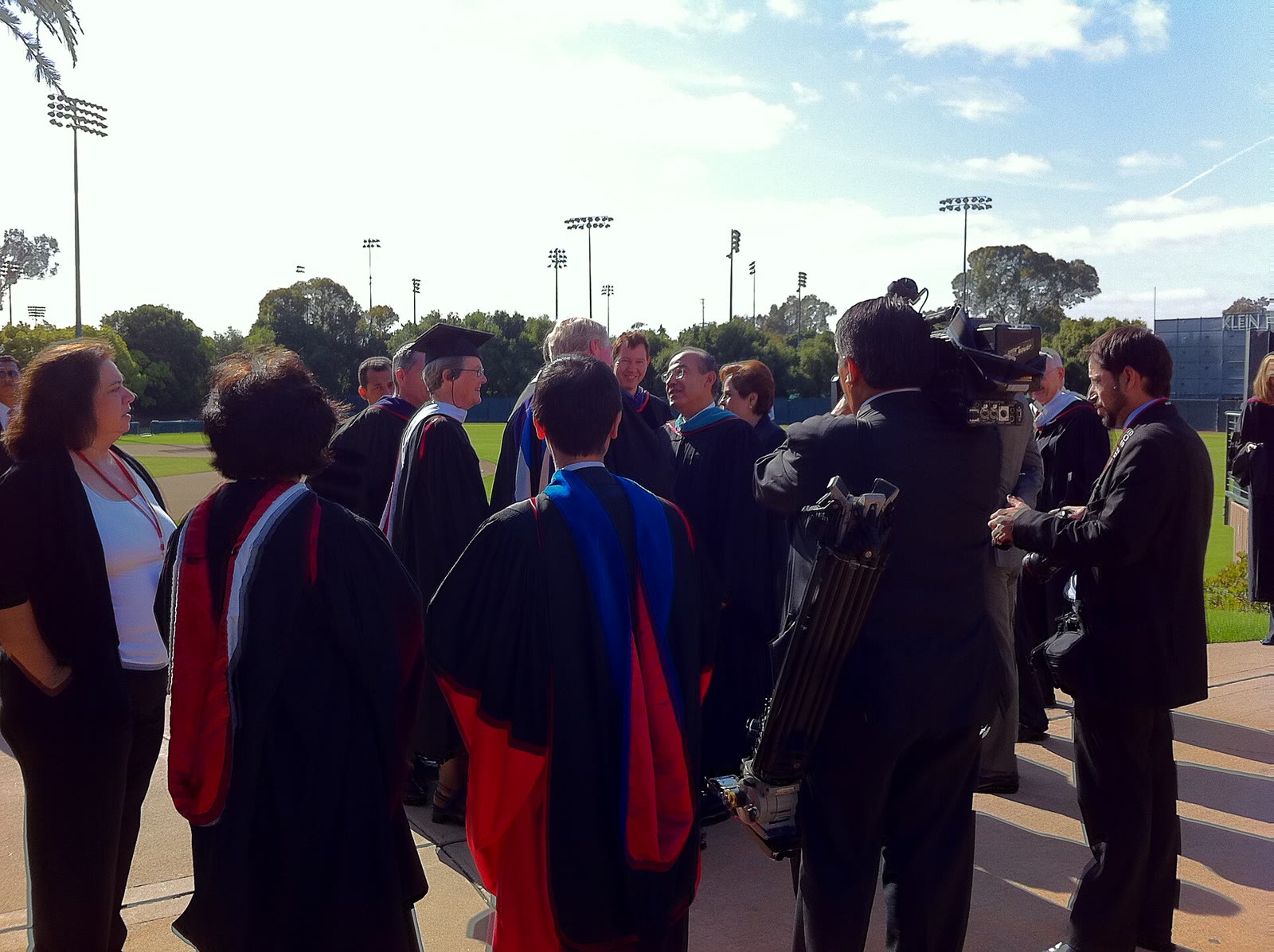 Graduates in black gowns and coloured hoods gathered on a field at Stanford University