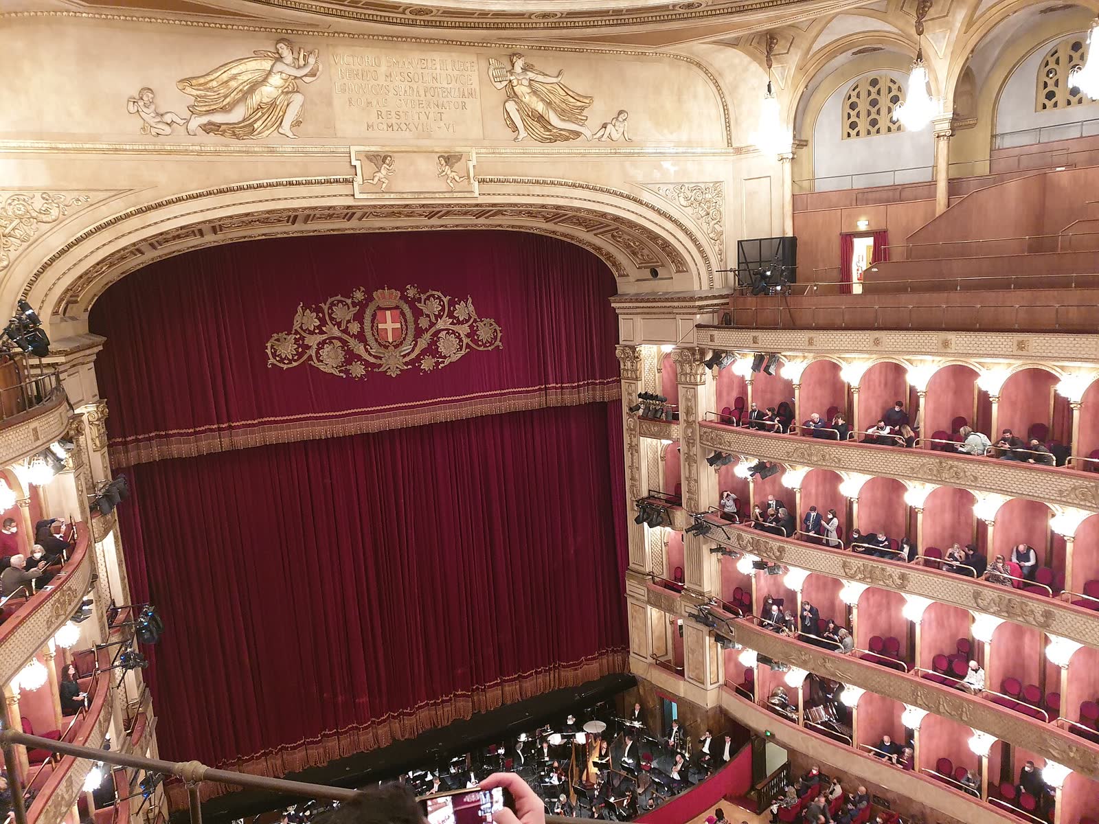 View from the top gallery of a red and gold opera house, with tiers of boxes and a red stage curtain