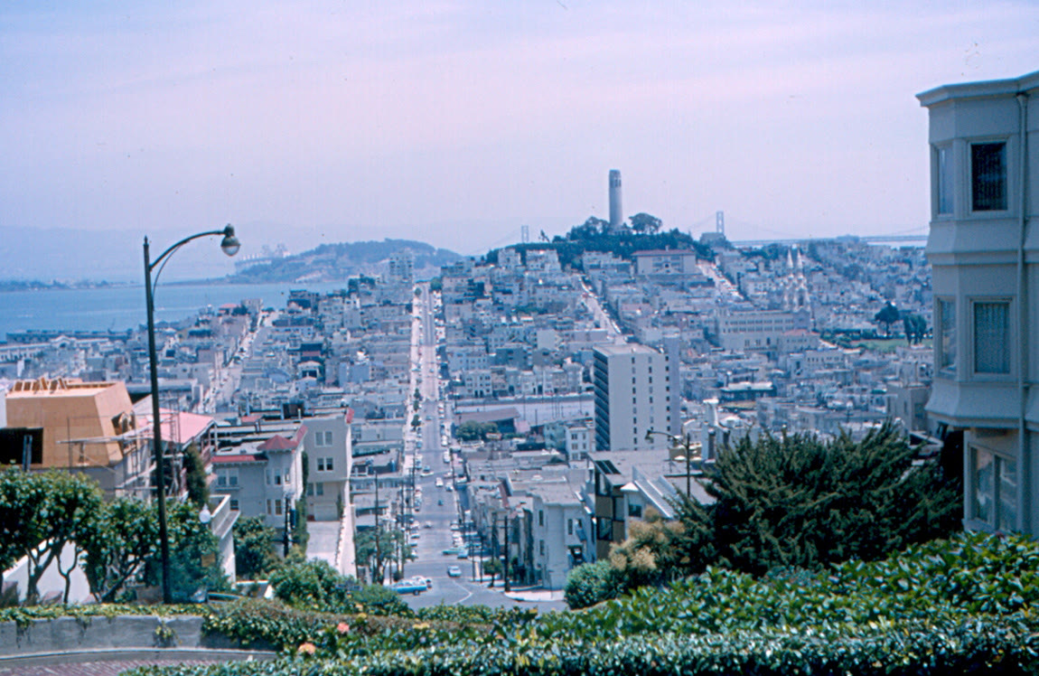 View down a long San Francisco street toward Telegraph Hill and Coit Tower, with the bay behind