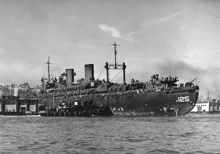 Black and white photograph of the troopship USS Admiral H. T. Mayo crowded with servicemen as it comes alongside a Fort Mason pier