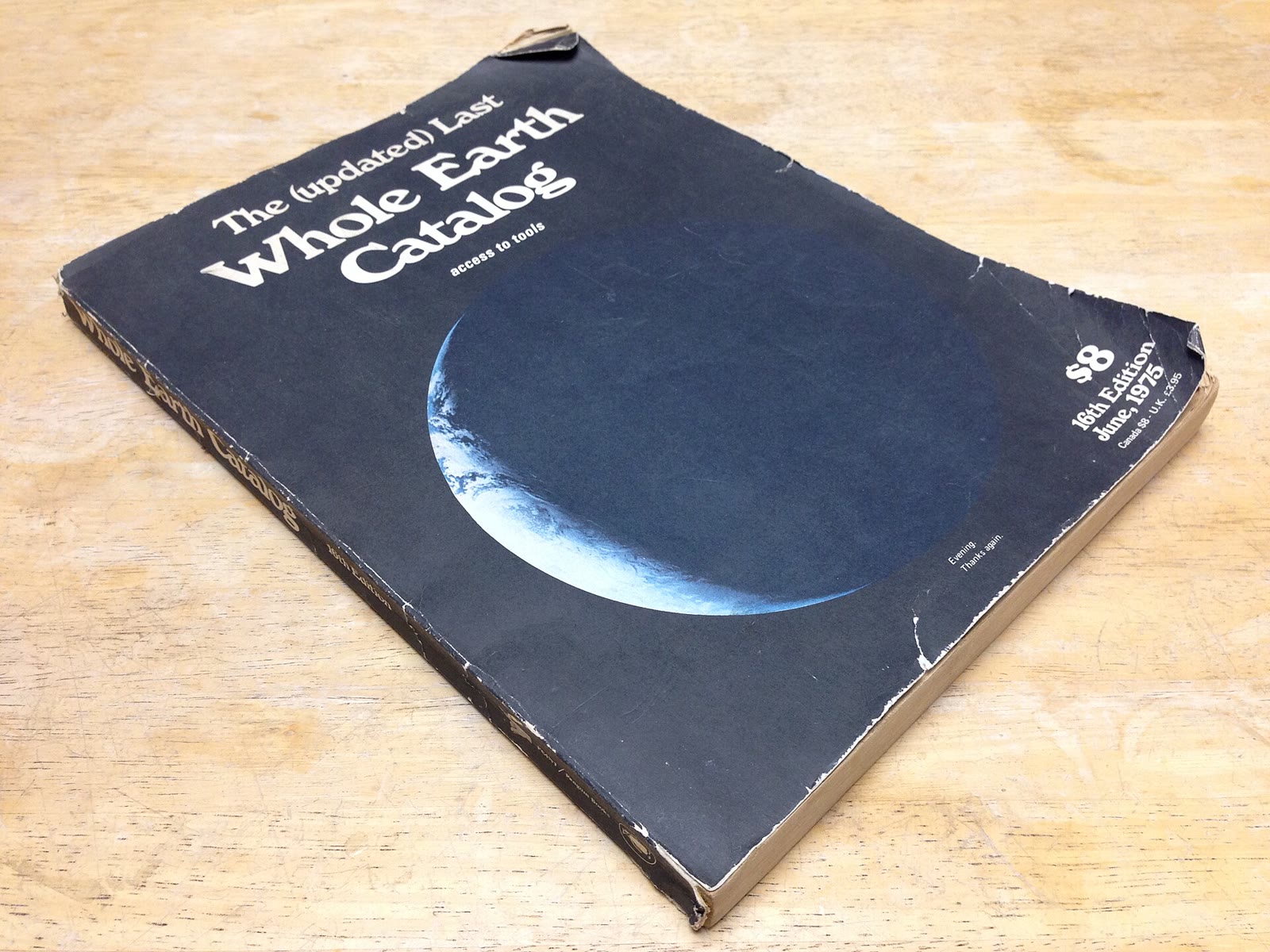 Worn black paperback copy of The (Updated) Last Whole Earth Catalog on a wooden table